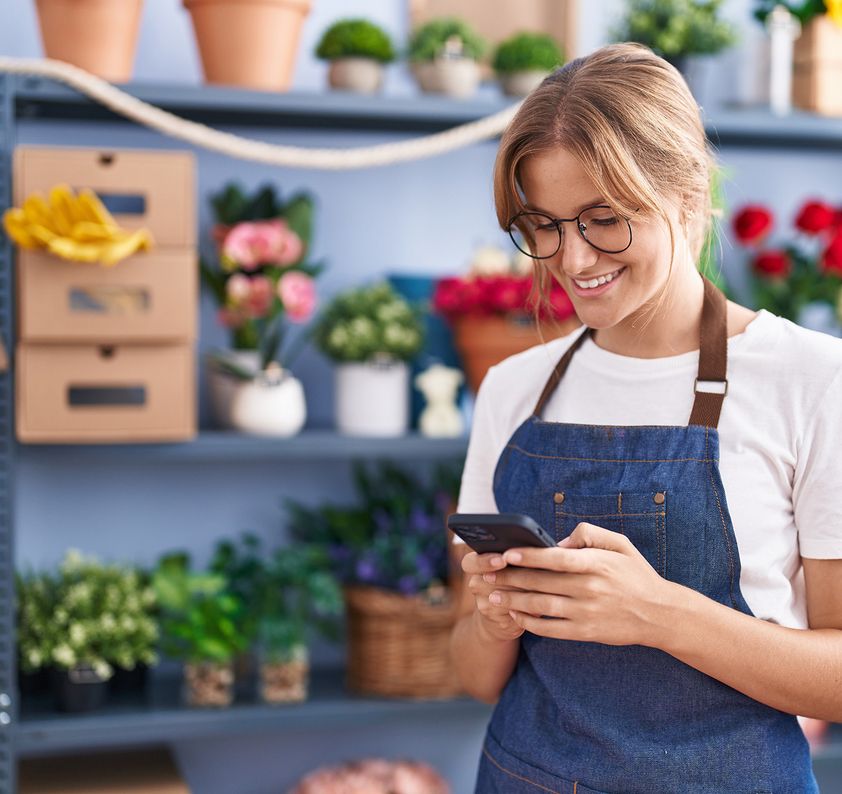Glückliche Floristin mit Smartphone im Blumenladen