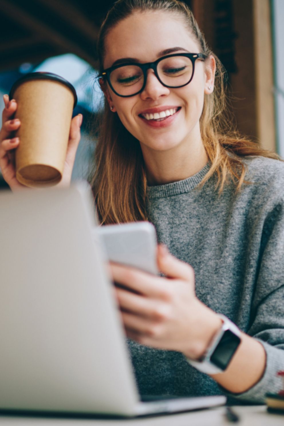 Eine Frau mit Brille genießt ihren Kaffee und nutzt ihren Laptop