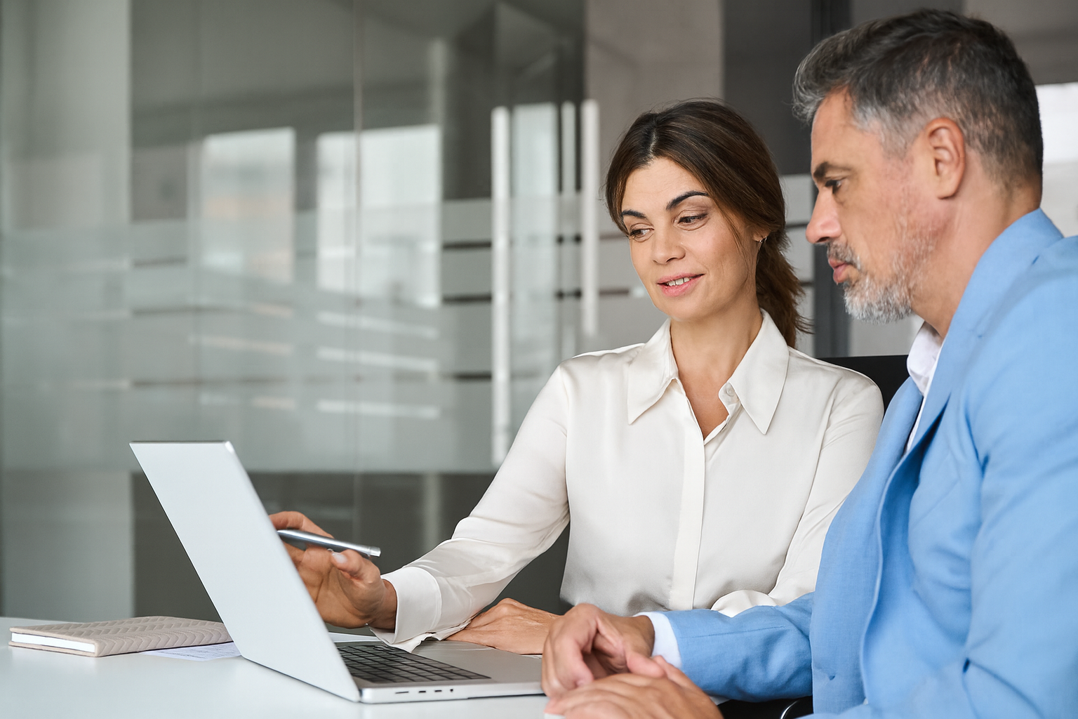 Zwei Personen sitzen im Büro und besprechen Inhalte auf einem Laptop-Bildschirm.